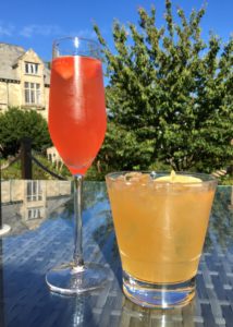 Two cocktails. One is pink in a flute and one is yellow in a cloudy tumbler.