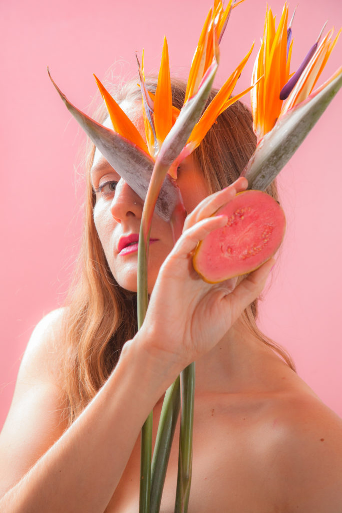 Woman in front of a pink background holding an orange flower and grapefruit