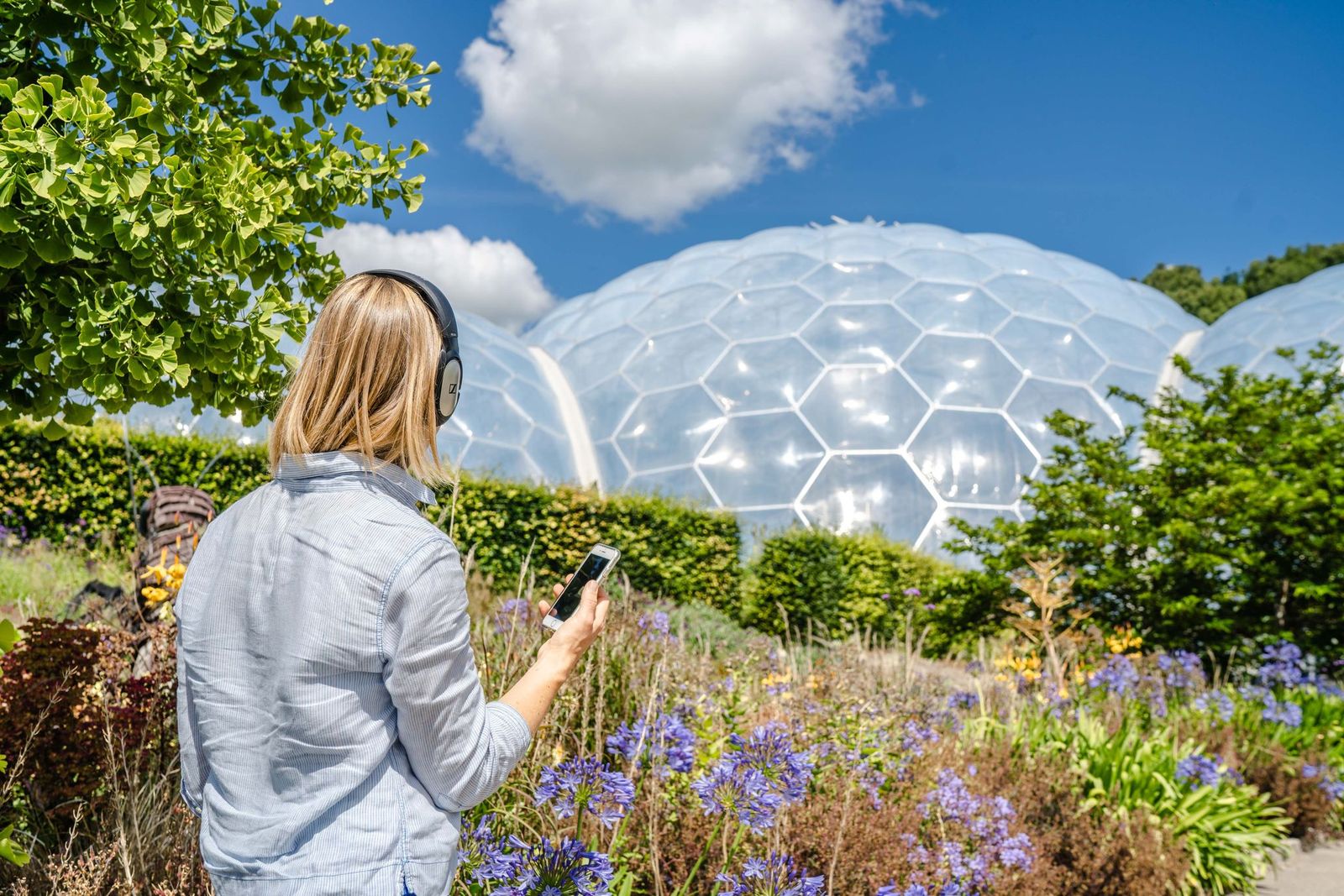 Woman listening to her smart phone through headphones outside the Eden Project domes