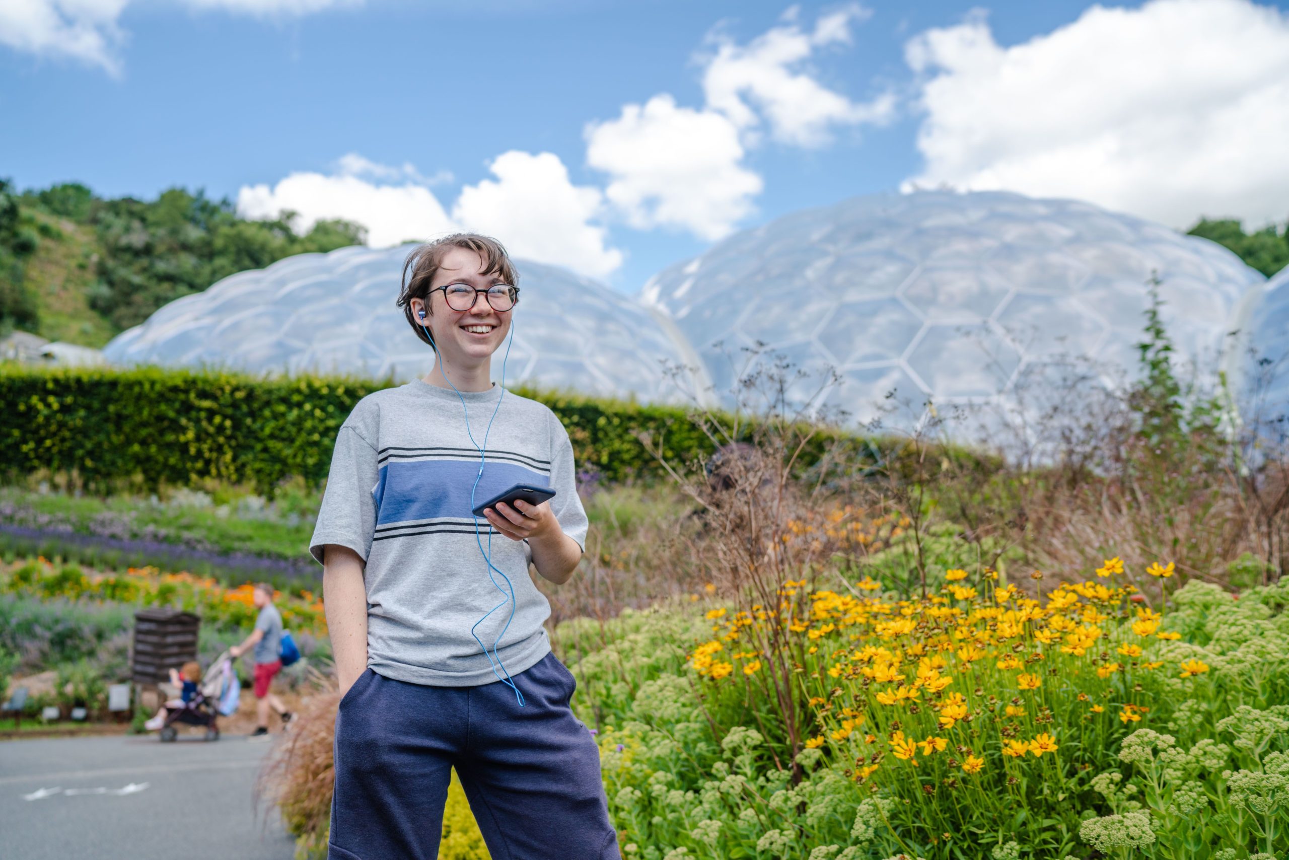 Boy listening to phone through headphones in front of the Eden Project domes