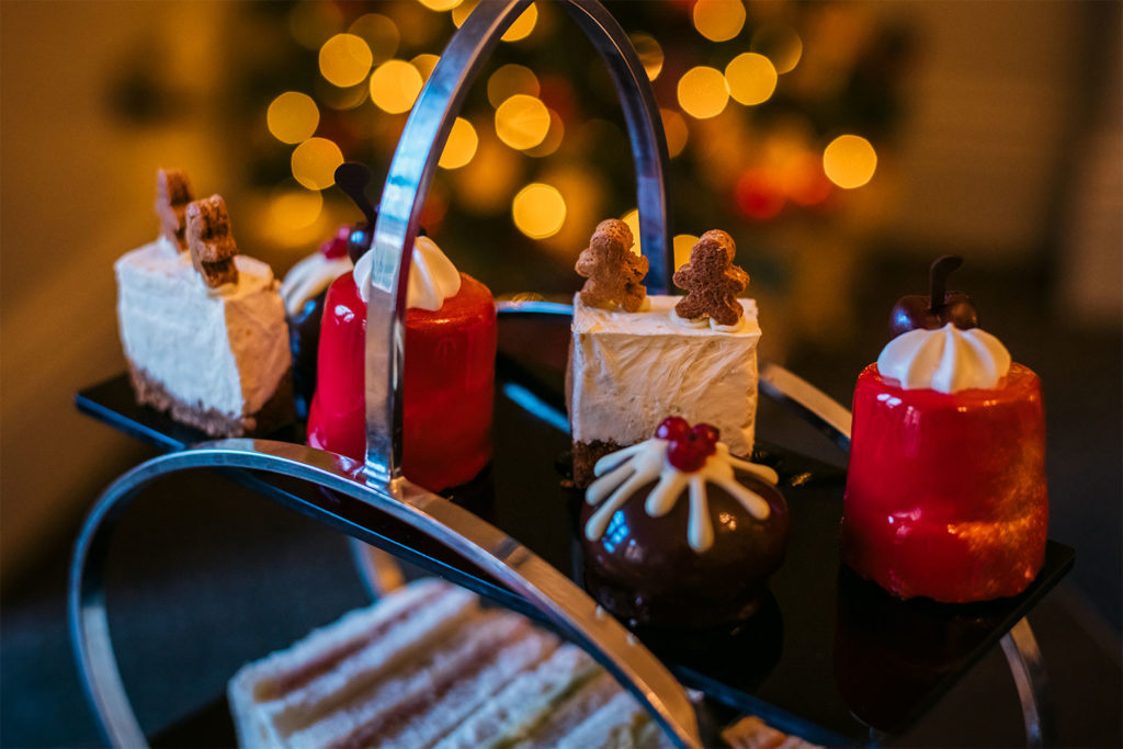 A table is set with a large circular stand which holds neat, small sandwiches, and perfectly tiny, festive cakes and pastries for afternoon tea.