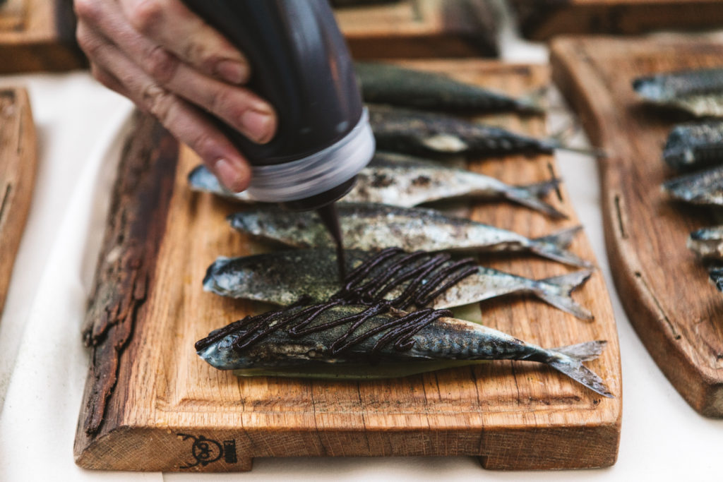 Someone is dressing whole fish with a black sauce in a squeezy bottle