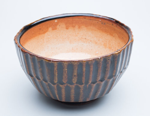 A brown and orange bowl with striking lined patterns on the outside