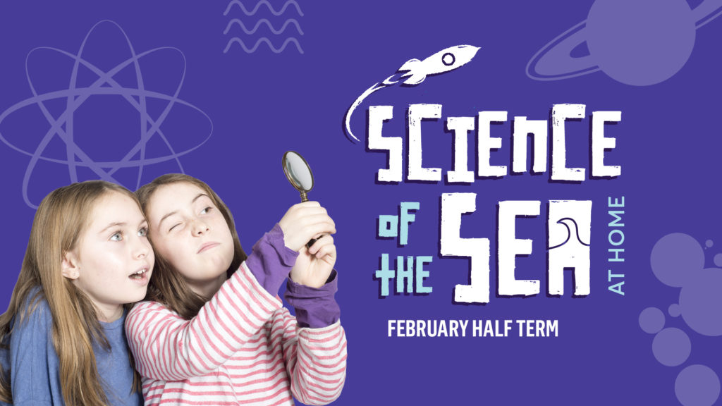 Two girls are standing next to each other. The one on the right is holding a magnifying glass up in front of her, looking with one eye closed in a curious expression. The one on the left is looking over her shoulder, looking with wonder into the magnifying glass.