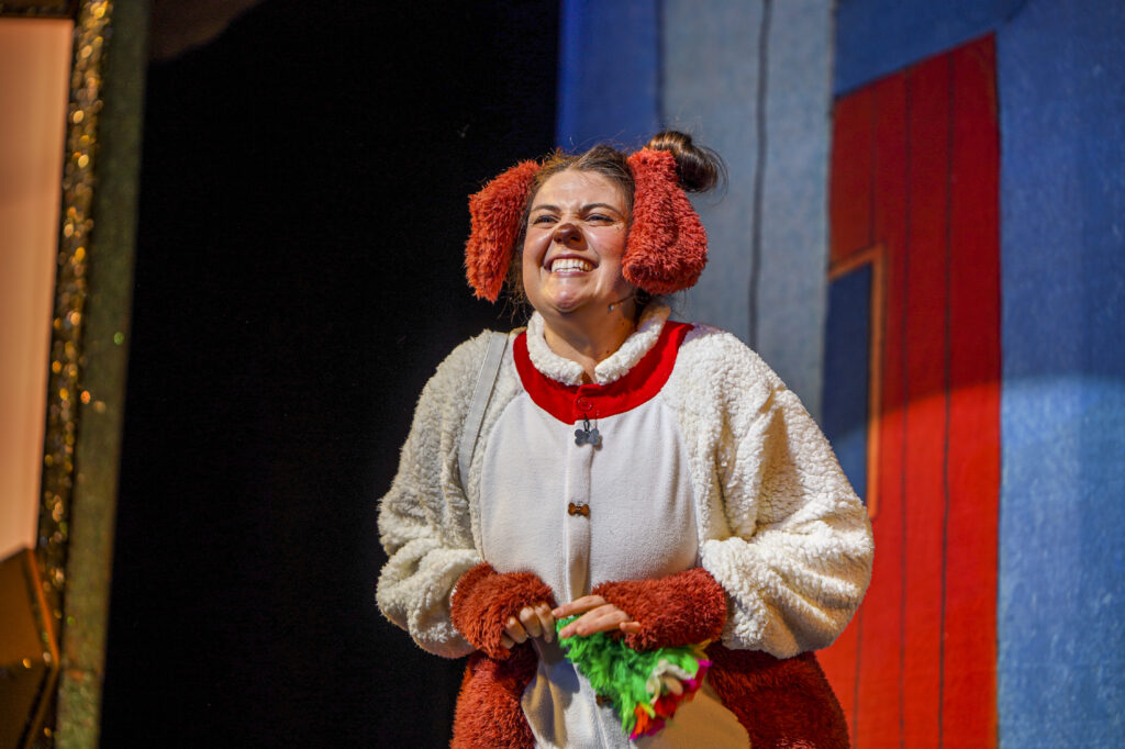 A woman dressed in a dog costume smiles at the audience 