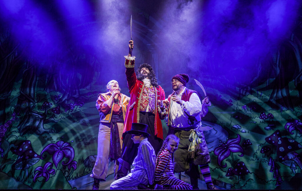 Three pirates stand in the middle of the stage. At their feet sit two children wearing pyjamas 