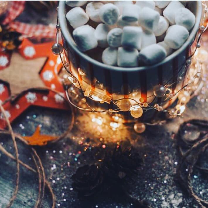 A hot chocolate topped with marshmallows is wrapped with festive glass beads and fairy lights.